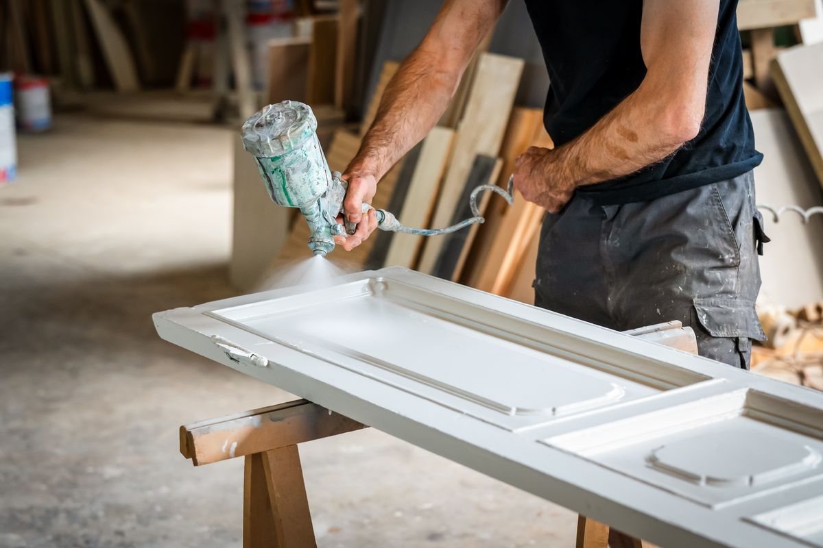 Person applying a white coating to a door laid across supports in a workshop