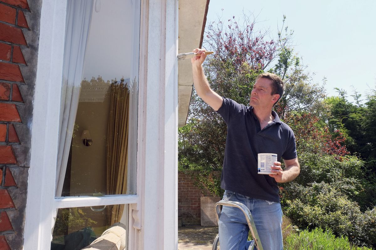 Painter on a stepladder brushing paint onto exterior window trim