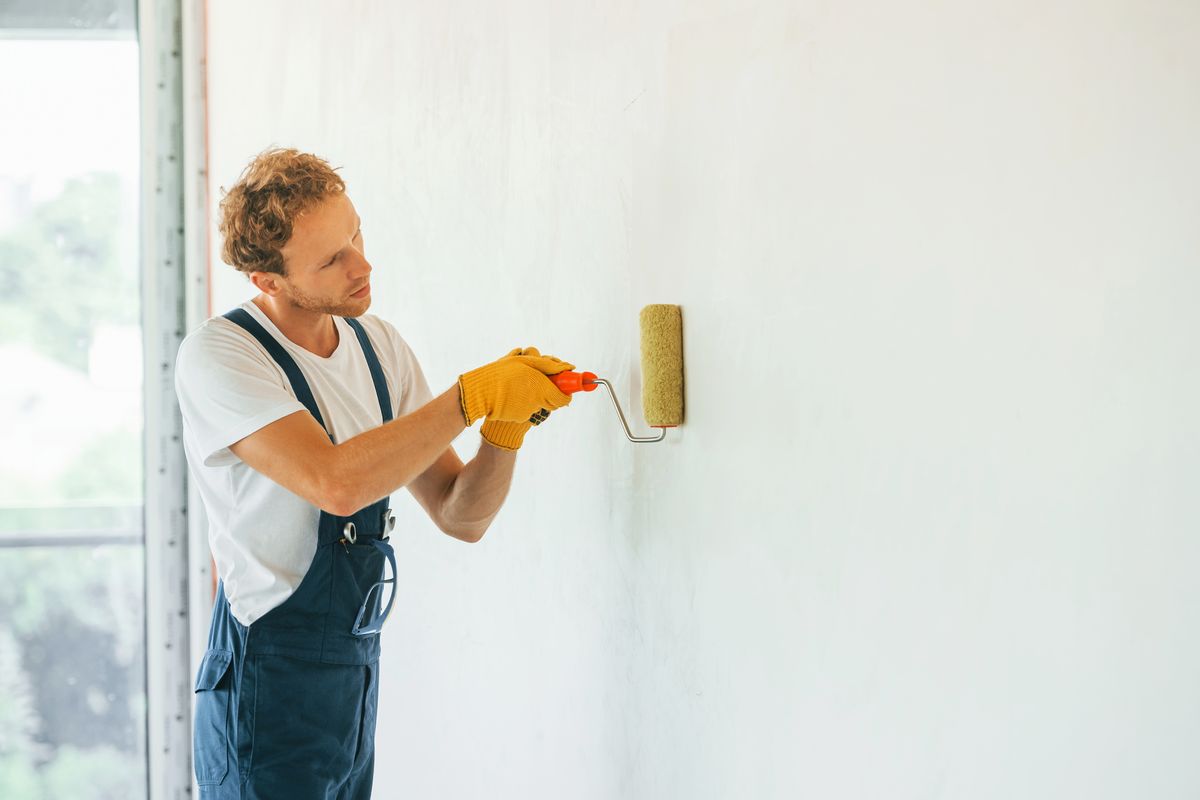Painter in overalls rolling white paint onto an interior wall