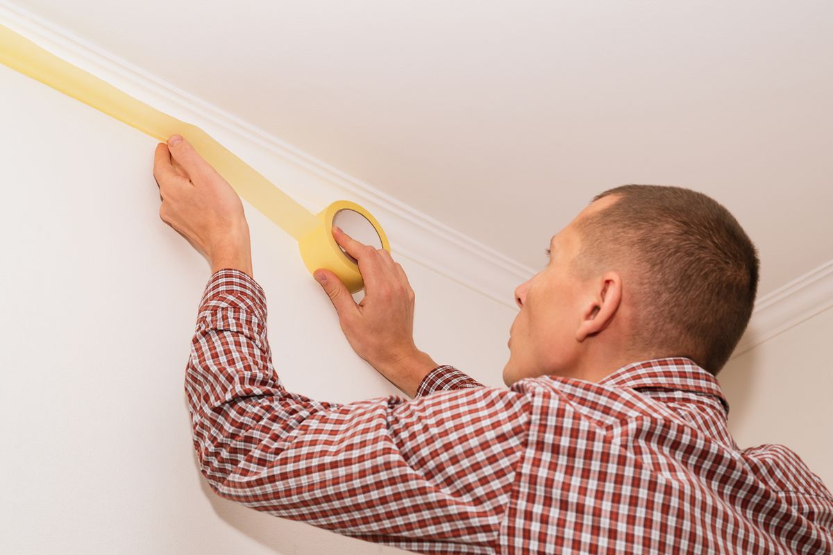 Person placing yellow masking tape along the edge of an interior wall