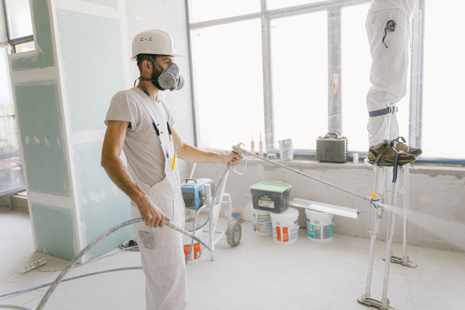 Commercial painter in whites spraying an interior wall in a bright office space