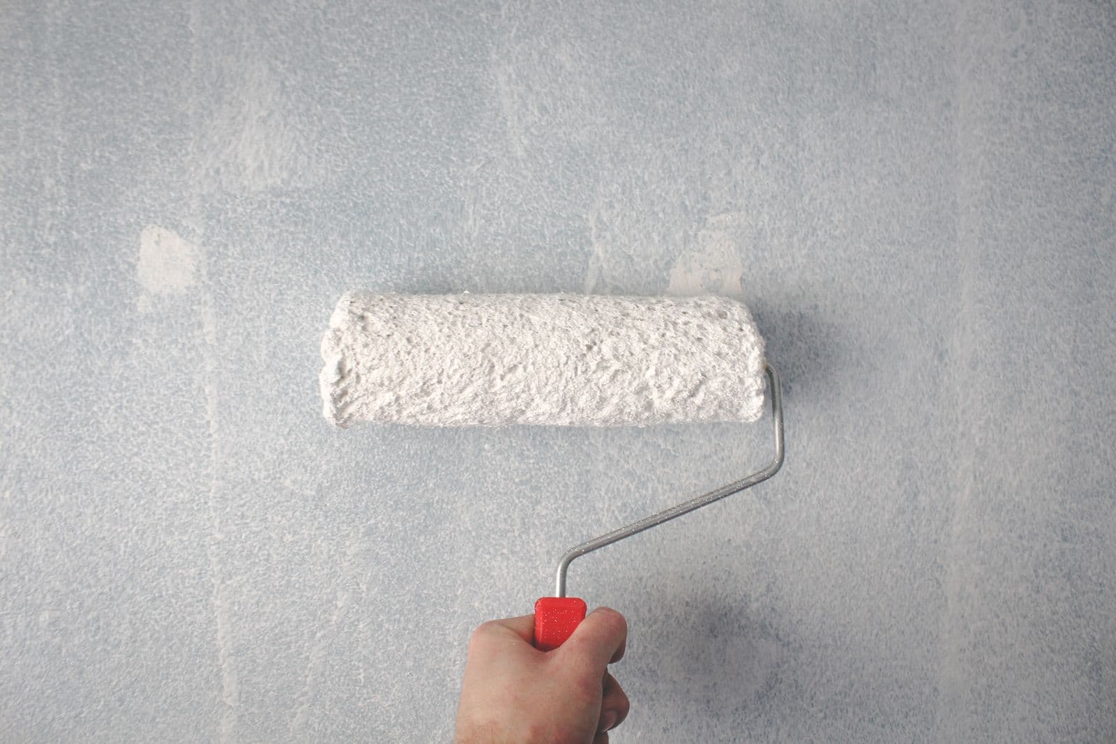 Painter rolling a smooth finish coat onto an interior wall with a paint roller