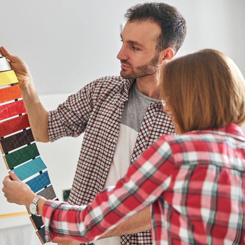 Two people comparing a fan of paint color samples beside a wall
